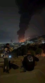 אזרחים איראנים מנגנים בגיטרות כשברקע עשן מתקיפות אוויריות....