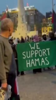 קבוצה מפגינים קטנה בכיכר "הדאם" באמסטרדם מרימה שלט ובו כתוב...