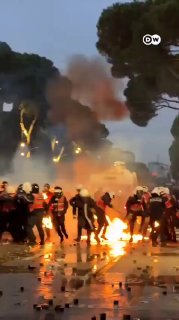 אש אוחזת ברגלו של שוטר באלבניה לאחר שנפגע מבקבוק תבערה. תודה...